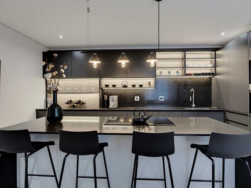 Modern kitchen featuring a central island with induction hob, sleek dark cabinetry, integrated appliances, and sophisticated under-cabinet lighting.
