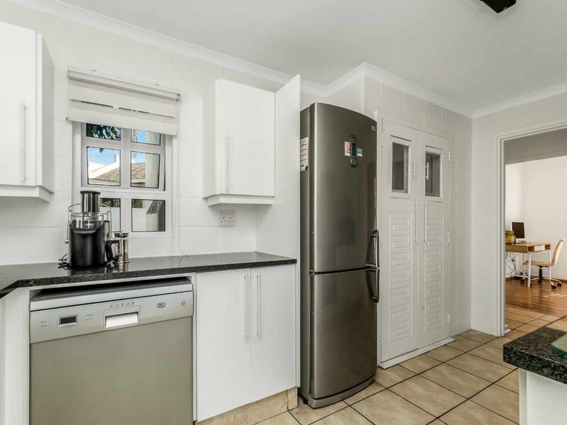 A clean, functional kitchen featuring white cabinetry, dark granite countertops, tiled walls, and modern stainless steel appliances, with a view into an adjacent office space.