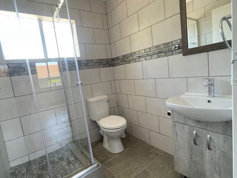 A clean and modern bathroom featuring a glass shower enclosure, a vanity cabinet with a basin, and neutral wall and floor tiling.