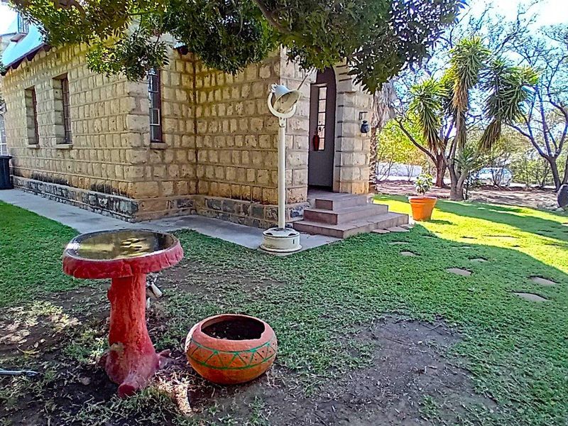 A view of the rear exterior featuring stone masonry walls, concrete entrance steps, and a well-maintained garden area with mature trees.