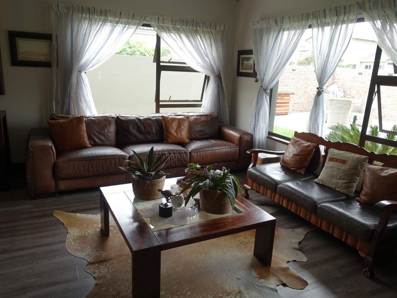 A comfortable living room featuring durable laminate flooring and large windows that provide ample natural light and views of the rear garden area.