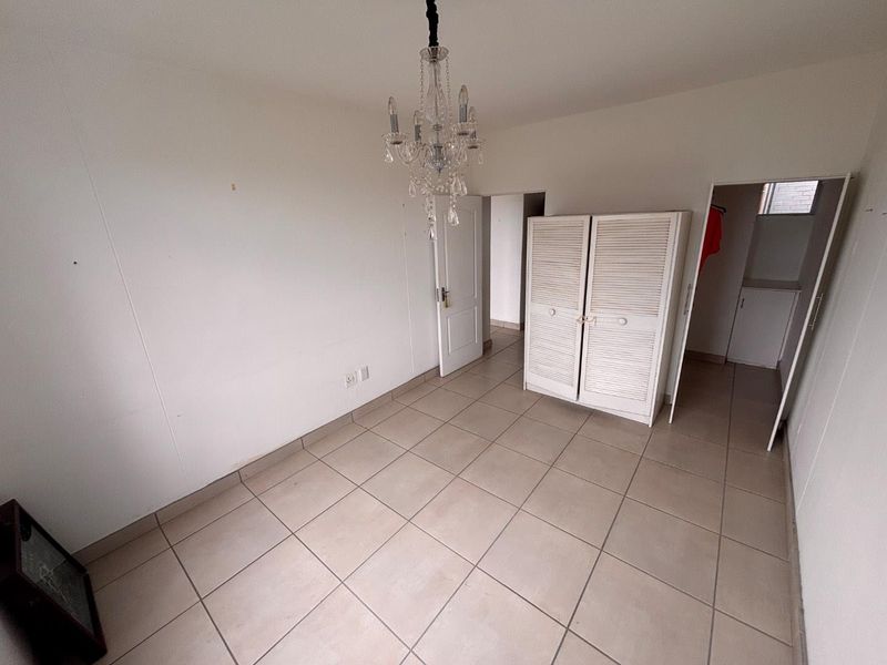 A vacant bedroom featuring neutral tiled flooring, a built-in cupboard, and a decorative chandelier, offering a blank canvas for personalization.