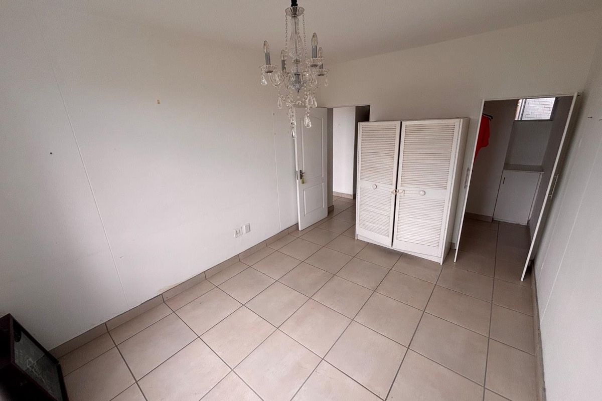 A vacant bedroom featuring neutral tiled flooring, a built-in cupboard, and a decorative chandelier, offering a blank canvas for personalization.