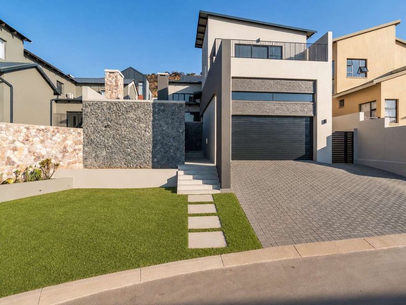 Modern multi-level residential facade featuring stone cladding, a paved driveway, double garage, and an upper-level balcony with metal railings.