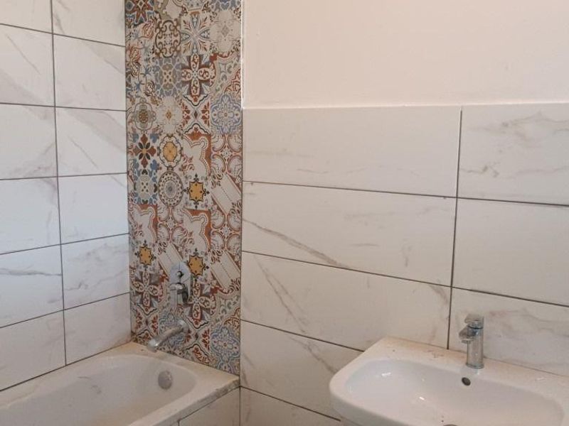A bathroom under renovation featuring a bathtub, wall-mounted basin, and decorative accent tiling. The space requires finishing touches to complete the installation.