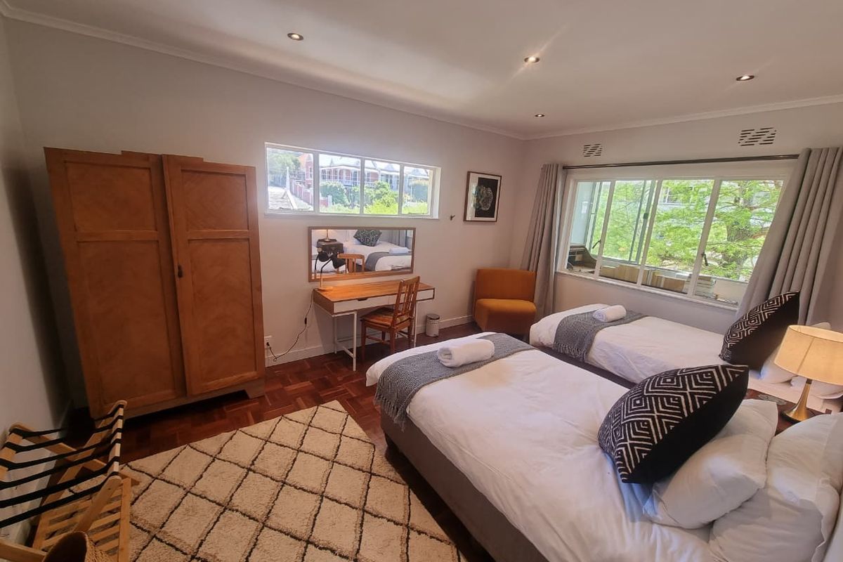 A well-lit bedroom featuring parquet flooring, large windows providing natural light, and recessed ceiling lighting.