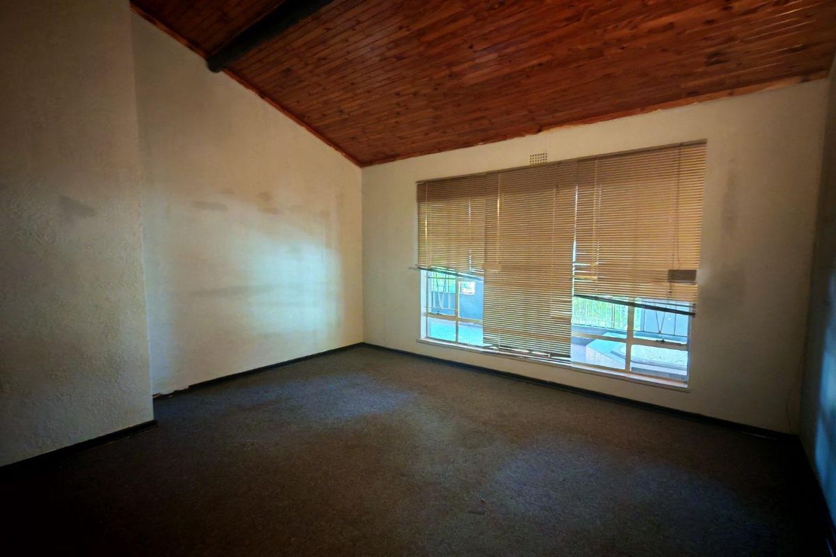 An empty bedroom featuring a vaulted timber ceiling, carpeted flooring, and large windows with fitted blinds.