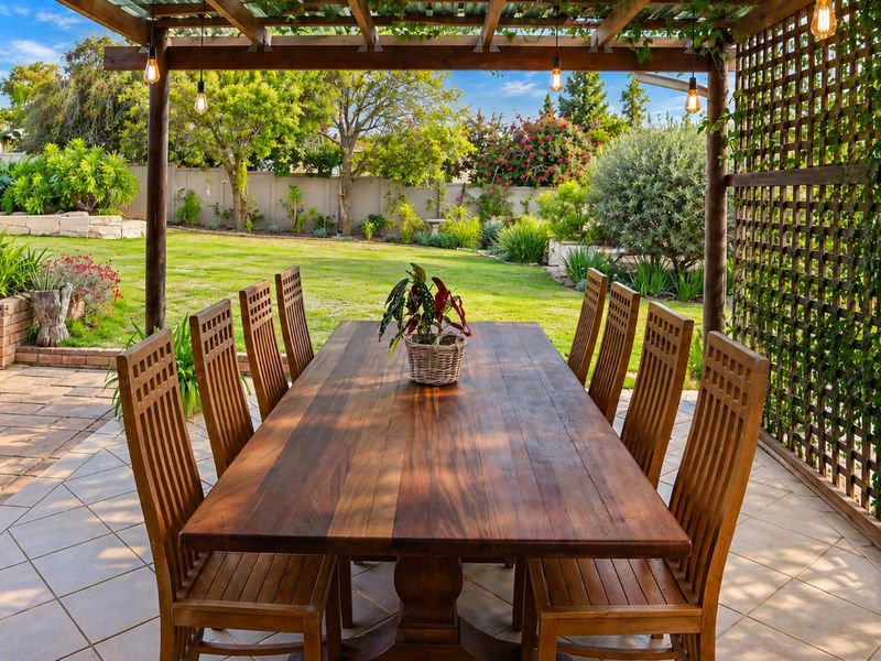 Covered outdoor patio featuring a timber pergola, tiled flooring, and a lattice privacy screen, overlooking a well-maintained garden.