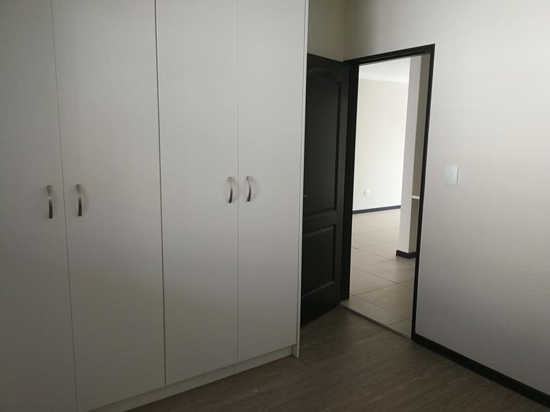 A clean, empty bedroom featuring modern built-in cupboards, neutral tiled flooring, and a dark-toned internal door leading to an adjacent living space.