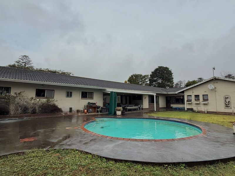 Rear view of the property featuring a swimming pool, concrete patio area, and brick exterior walls under a tiled roof.
