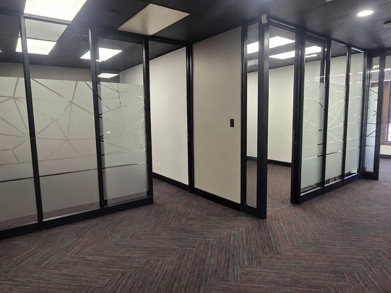 Modern office space featuring glass partition walls, recessed lighting, and high-quality carpet flooring, providing a professional and bright work environment.