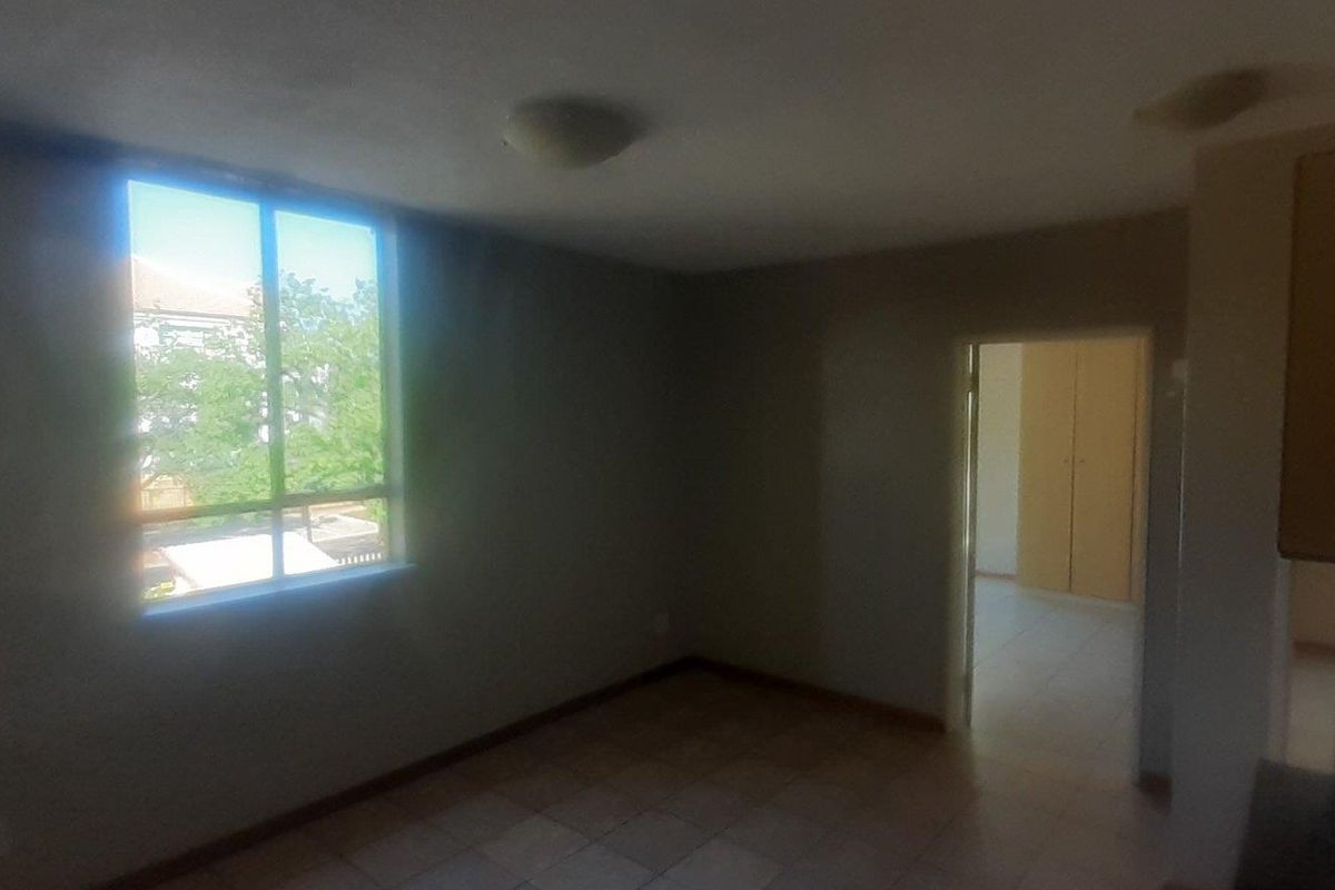 An empty living area featuring tiled flooring, a large window providing natural light, and access to an adjacent room with built-in cupboards.