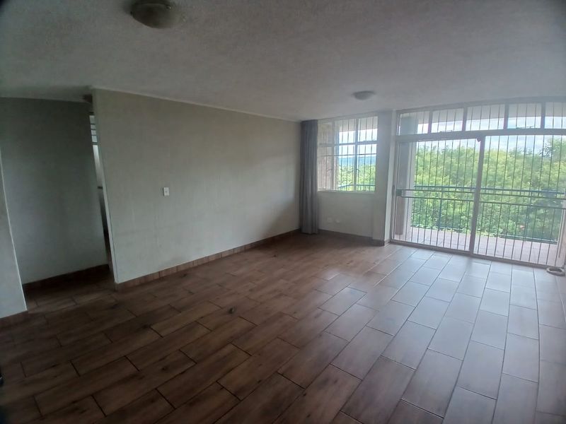 Spacious, empty living area featuring wood-look tiled flooring and large sliding glass doors that open to a balcony with scenic views.