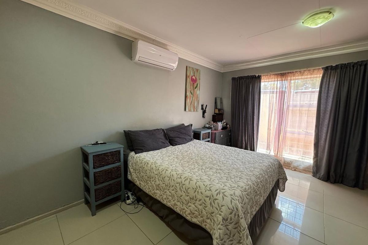A well-lit bedroom featuring tiled flooring, crown molding, and a wall-mounted air conditioning unit with direct access to the exterior.