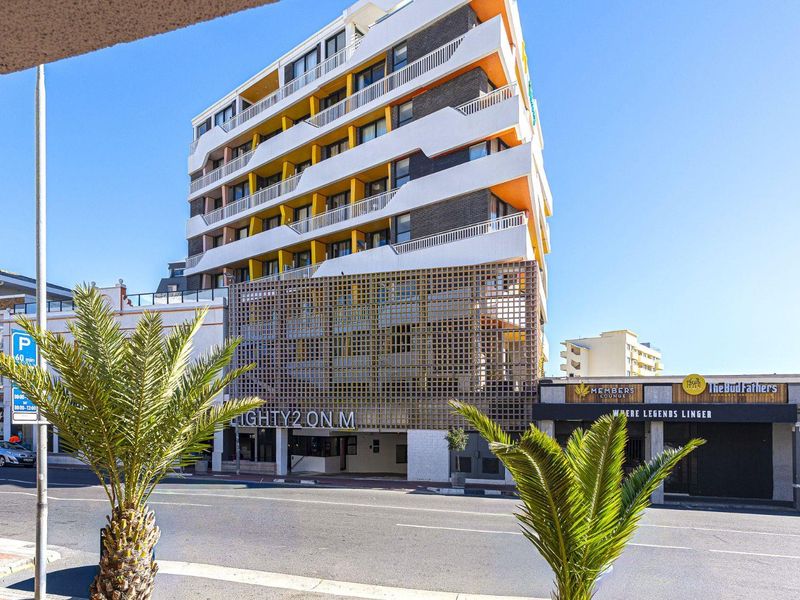 A modern multi-story apartment building facade featuring distinctive yellow accents, private balconies, and a decorative architectural lattice screen at street level.