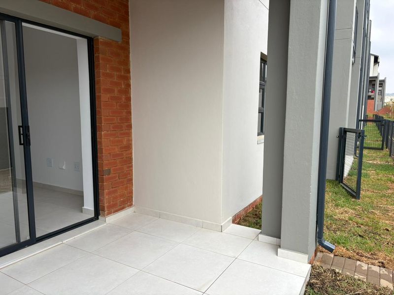 A modern covered patio featuring tiled flooring, a sliding glass door entrance, and a combination of brick and plastered exterior finishes.