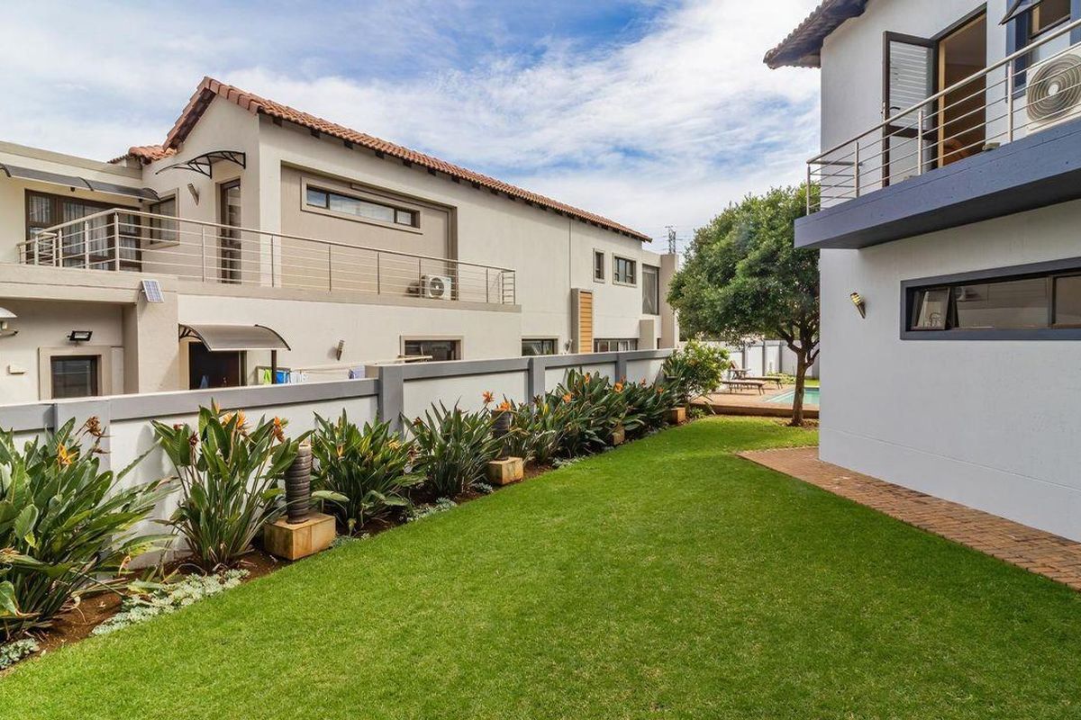 A well-maintained rear garden area featuring a manicured lawn, landscaped garden beds, and paved pathways between the residential structures.