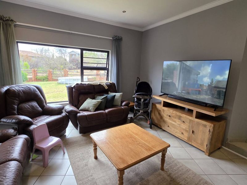 A comfortable living room featuring tiled flooring, large windows providing natural light, and neutral wall finishes.