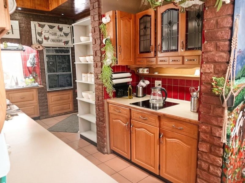 A traditional kitchen featuring warm-toned wooden cabinetry, red tiled backsplash, and exposed brick architectural elements, providing a rustic and functional cooking space.