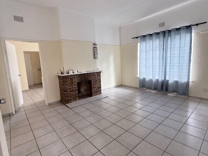 Spacious living room featuring tiled flooring and a traditional brick fireplace, offering a blank canvas for renovation and interior design updates.