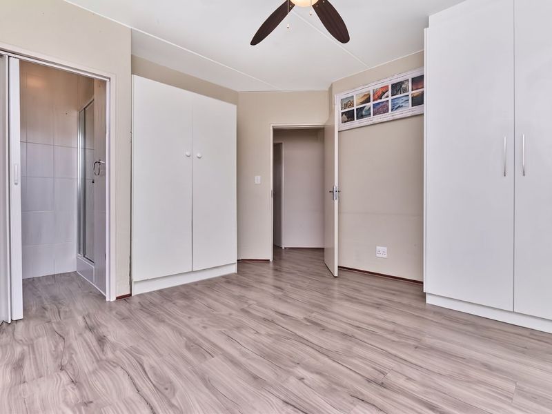 A bright, empty bedroom featuring modern laminate flooring, built-in cupboards, a ceiling fan, and direct access to an en-suite bathroom.