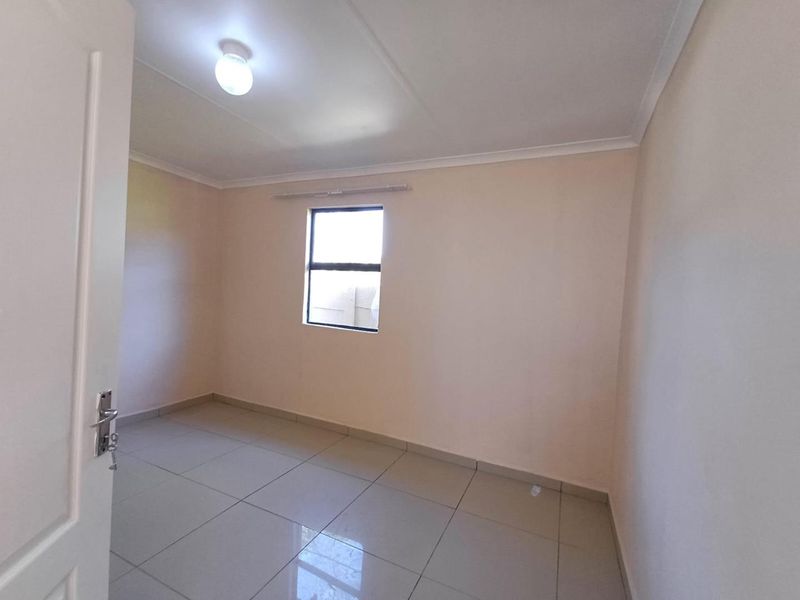 A clean, empty bedroom featuring neutral wall paint, large floor tiles, and a single window, providing a blank canvas for interior design.