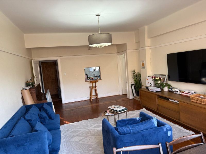 Spacious living room featuring original hardwood flooring, classic picture rails, and a convenient pass-through window connecting to the kitchen area.