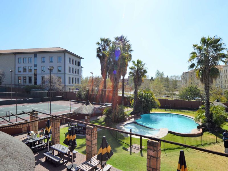 Communal outdoor area featuring a swimming pool, tennis court, and landscaped garden space within the apartment complex.