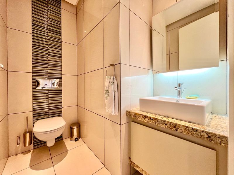 Modern bathroom featuring a wall-mounted toilet with concealed cistern, vessel sink on a granite countertop, and contemporary tiled wall finishes.