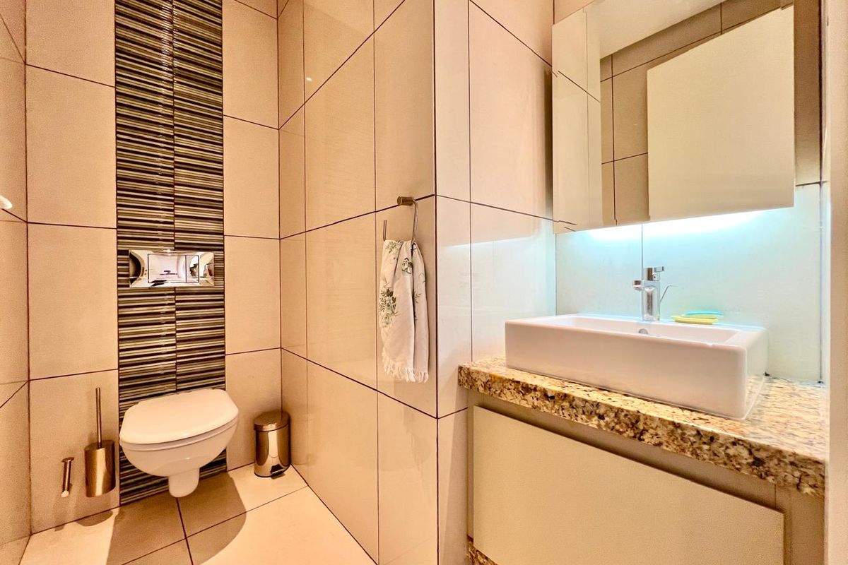 Modern bathroom featuring a wall-mounted toilet with concealed cistern, vessel sink on a granite countertop, and contemporary tiled wall finishes.