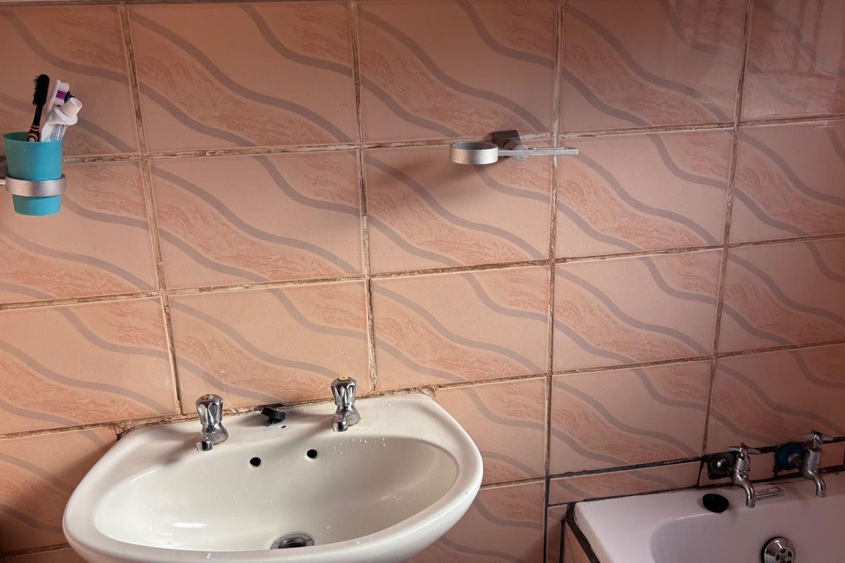 A dated bathroom vanity area featuring a wall-mounted basin, chrome taps, and patterned ceramic wall tiles.