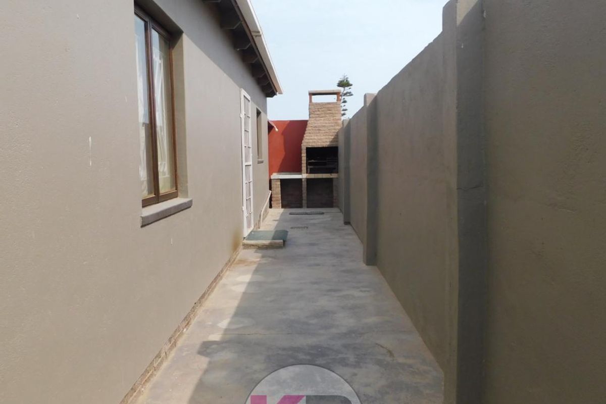 A side exterior walkway featuring a built-in brick braai area and high boundary walls, providing a private outdoor space.