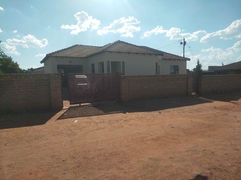 Front exterior view of a single-story house featuring a tiled roof, brick boundary wall, and a metal driveway gate.