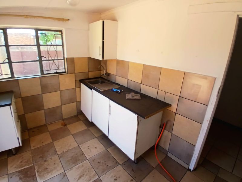 A compact kitchen area featuring built-in cabinetry, a stainless steel sink, and tiled finishes, offering a functional space ready for modernization.