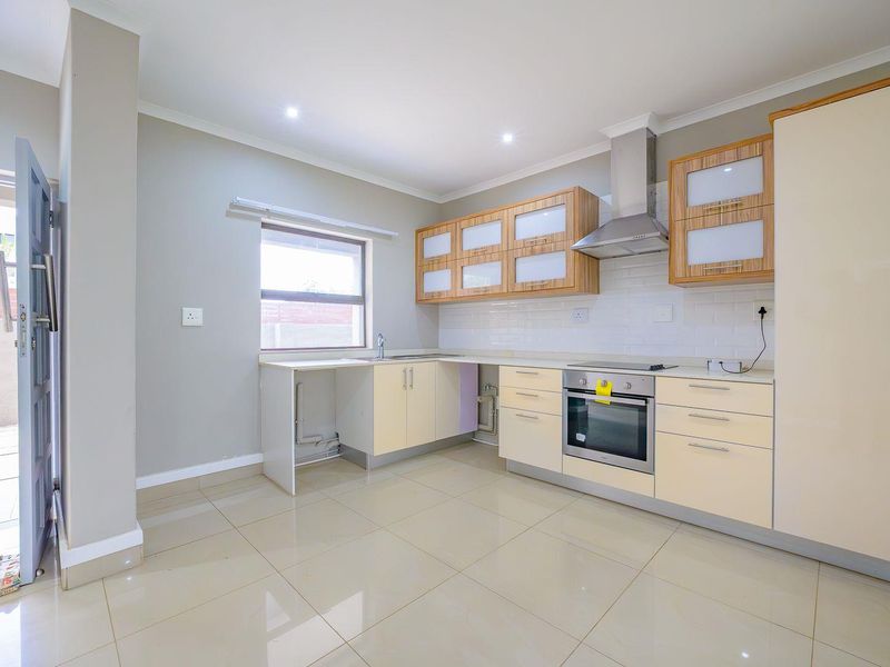 Modern kitchen featuring light-toned cabinetry, built-in oven and hob, extractor fan, subway tile backsplash, and tiled flooring with direct access to an outdoor area.