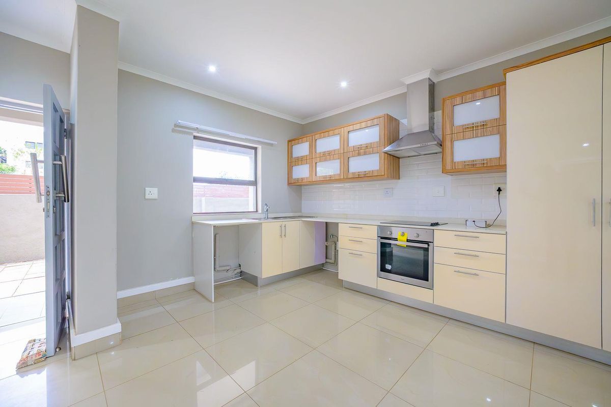 Modern kitchen featuring light-toned cabinetry, built-in oven and hob, extractor fan, subway tile backsplash, and tiled flooring with direct access to an outdoor area.
