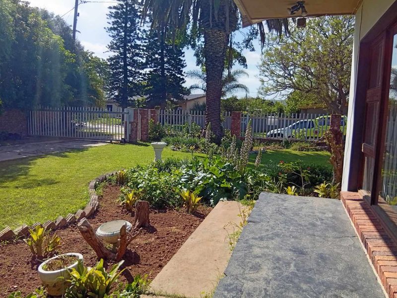 A view from the front patio looking out over a landscaped garden with a lawn, mature trees, and secure metal perimeter fencing.