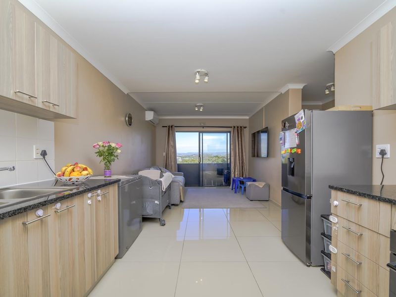 Open-plan kitchen and living area featuring modern laminate cabinetry, granite countertops, tiled flooring, and a sliding door leading to an outdoor balcony.