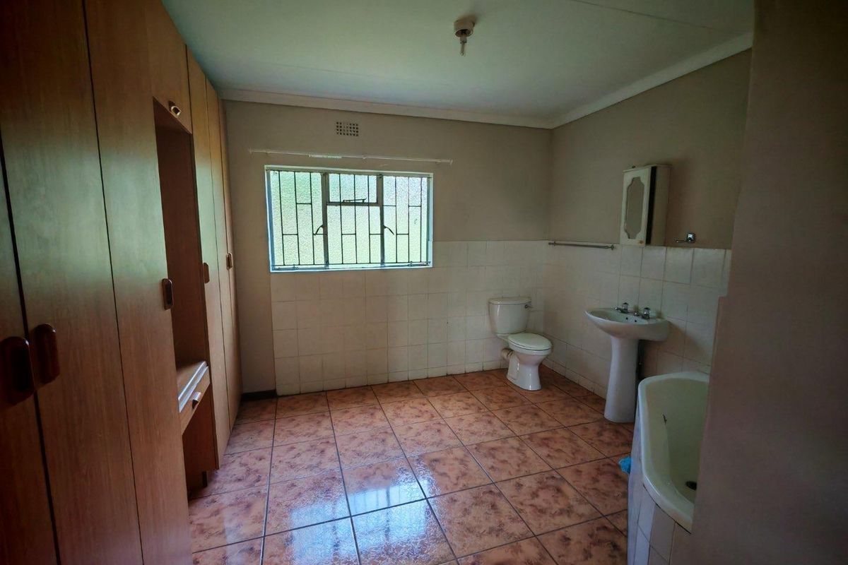 A spacious, dated bathroom featuring built-in wooden cabinetry, a pedestal basin, a toilet, and a bathtub with tiled flooring and wall surrounds.