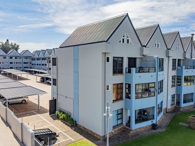 Aerial view of a modern apartment complex featuring multi-story units, covered parking bays, paved driveways, and well-maintained communal lawn areas.