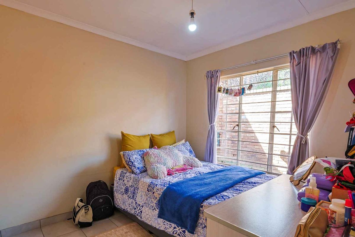 A standard bedroom featuring tiled flooring, a large window with security bars, and neutral wall finishes.