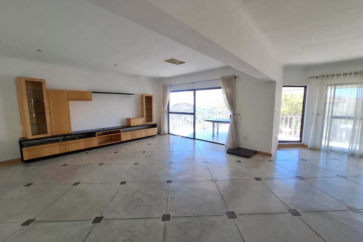 Spacious living area featuring large format tiled flooring, built-in cabinetry, and sliding glass doors providing access to an outdoor balcony with scenic views.