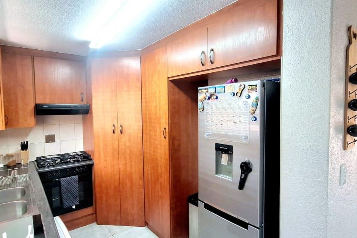 A functional kitchen featuring warm-toned wooden cabinetry, a gas stove with extractor fan, and a double basin sink, seamlessly connected to the living area.