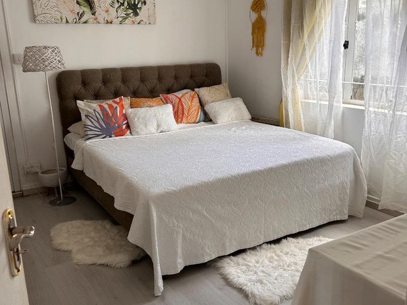 A well-lit bedroom featuring light-toned laminate flooring and a window with natural light, providing a comfortable and functional living space.
