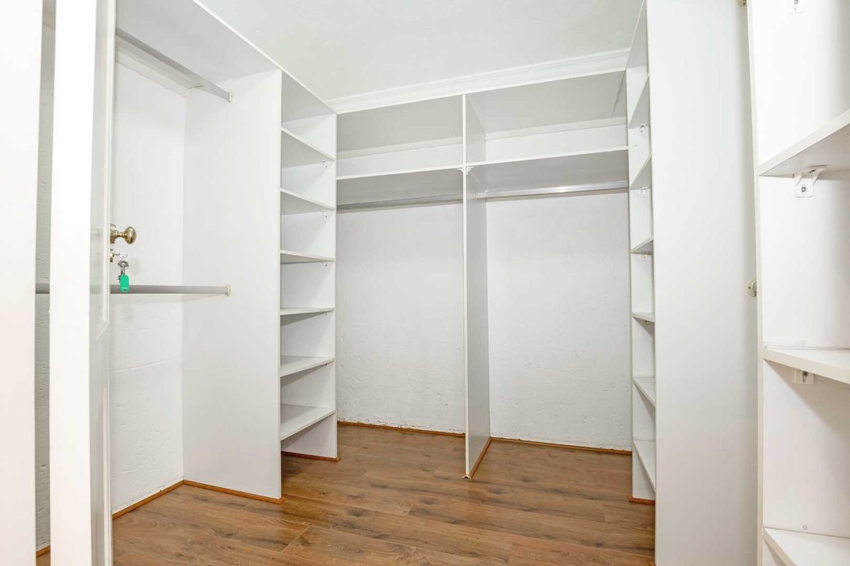 A walk-in closet featuring built-in white shelving and hanging rails, complemented by wood-look flooring.