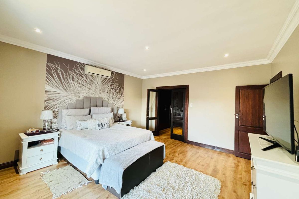 Spacious bedroom featuring laminate flooring, recessed ceiling lighting, crown molding, and a wall-mounted air conditioning unit.
