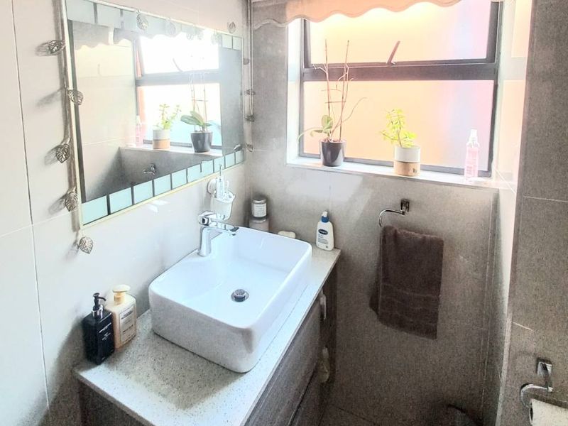 A modern bathroom featuring a vessel sink vanity, stone countertop, wall-mounted mirror, and neutral grey floor-to-ceiling tiling.