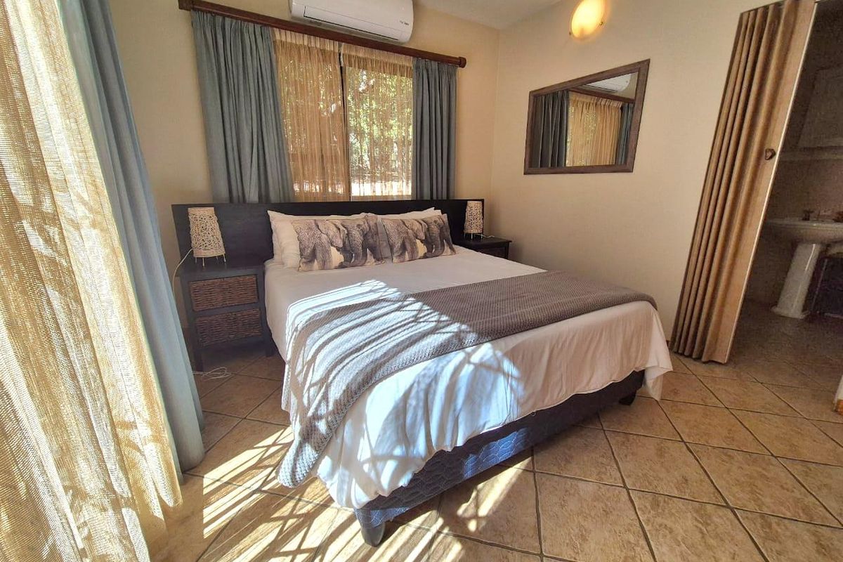 A comfortable bedroom featuring tiled flooring, a wall-mounted air conditioning unit, and an adjoining en-suite bathroom area.