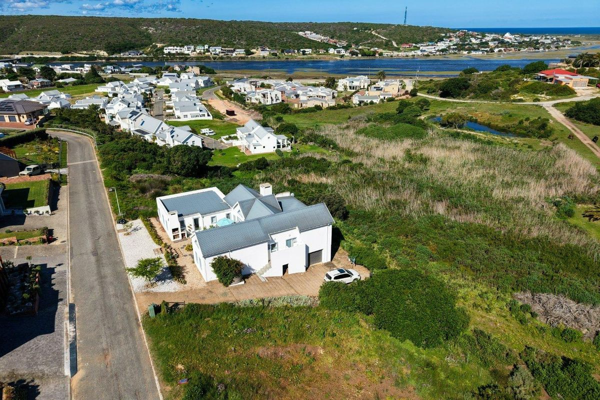 Aerial view of a white residential house with a metal roof, featuring a paved driveway and garage, situated in a coastal estate setting.
