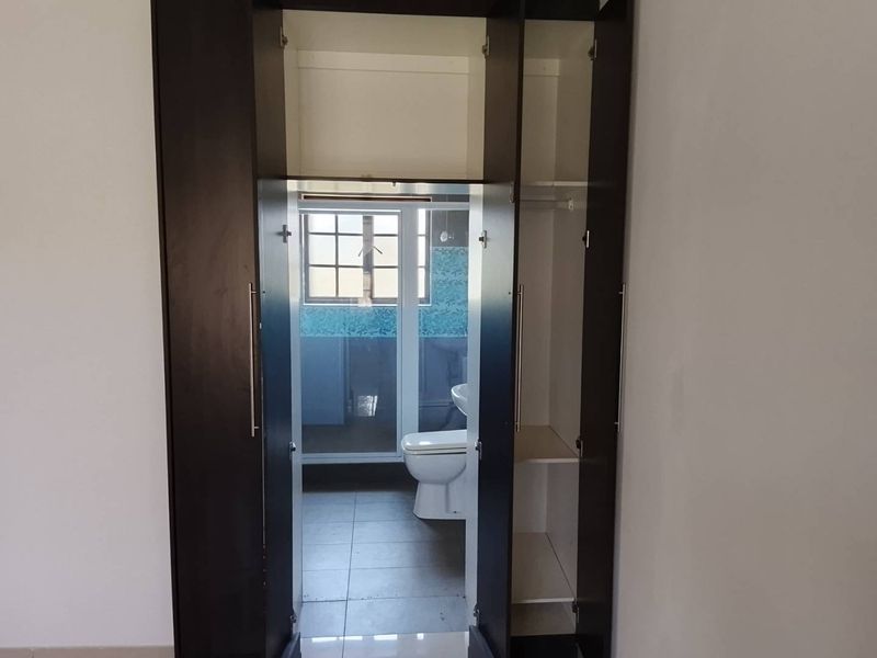 A bedroom featuring built-in dark wood cupboards with direct access to an en-suite bathroom with tiled flooring.